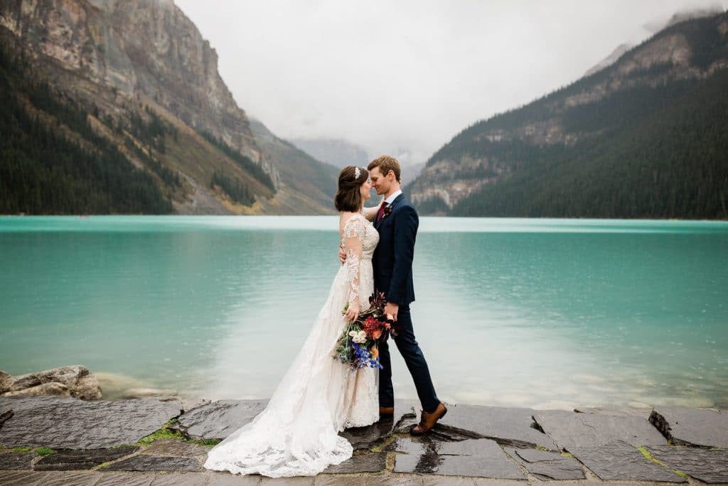 Lake Louise wedding portrait photograph of a bride and groom holding each other on the shoreline of the famous Lake Louise