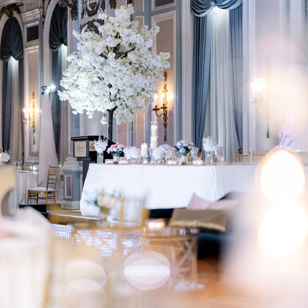 A luxurious wedding reception setup with large floral centerpiece, candlelit tables, and classic wall sconces in a grand hall.