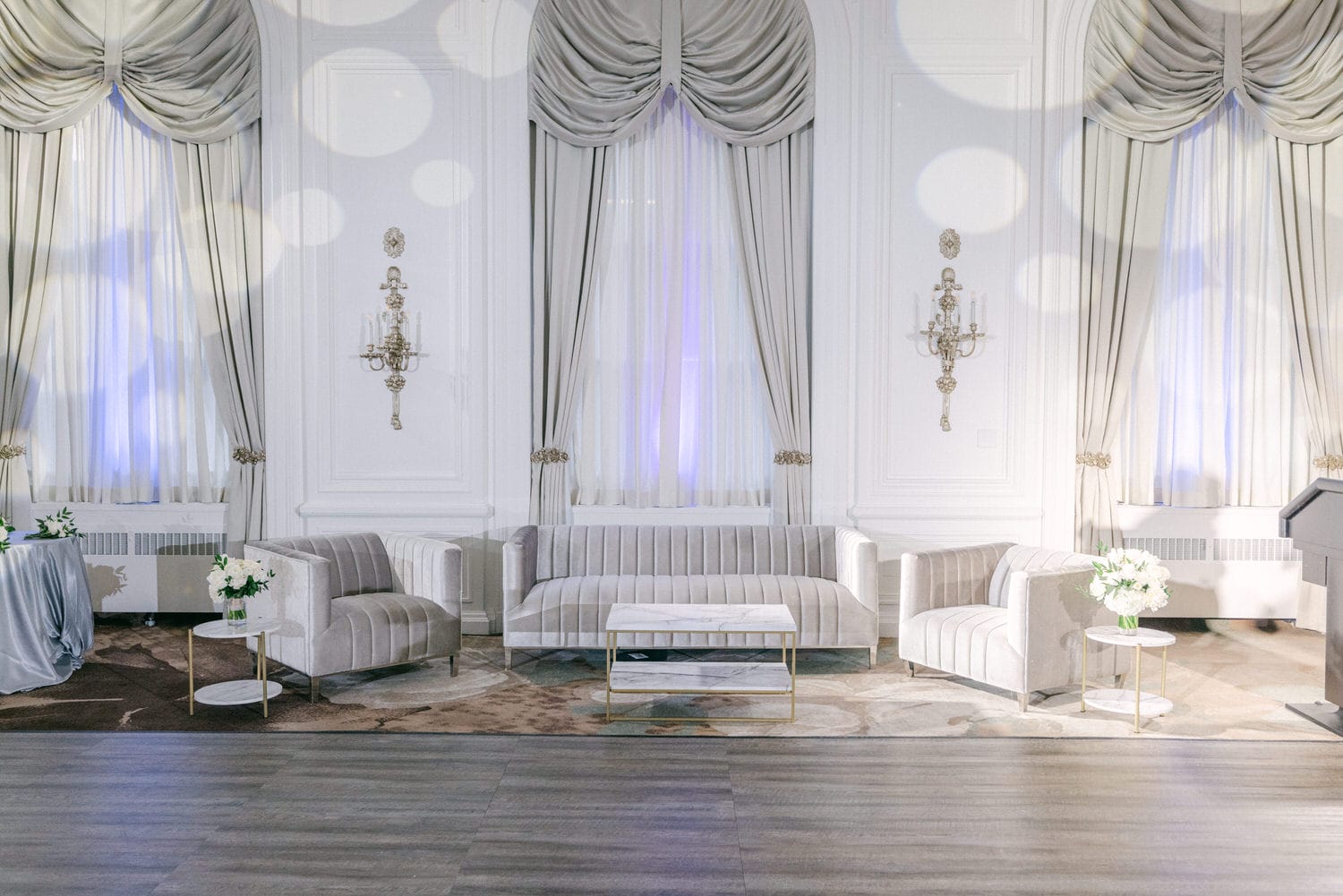 A sophisticated event space with plush seating, accent tables, and draped windows with ambient lighting.