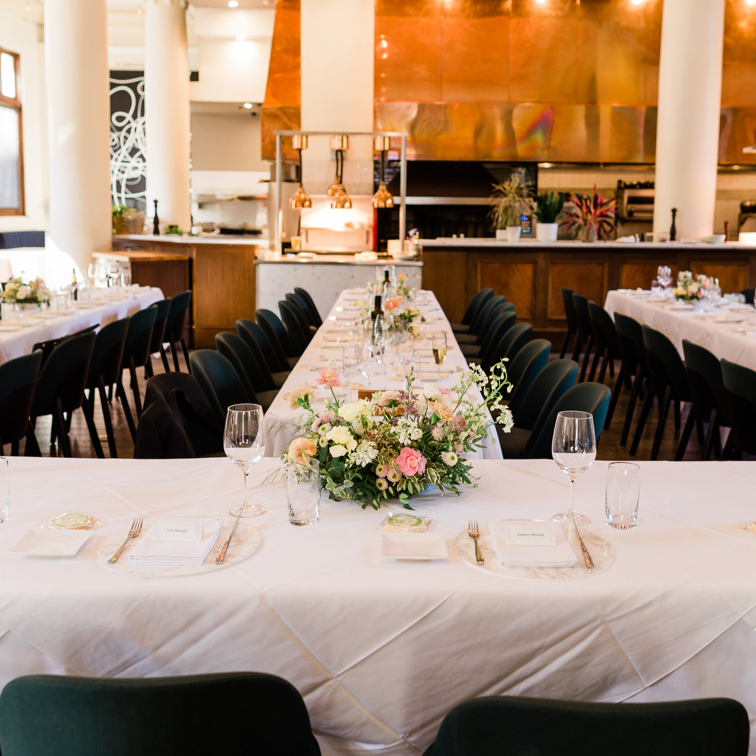 Long dining tables arranged with white linens, floral centerpieces, and place settings in a sophisticated restaurant interior.