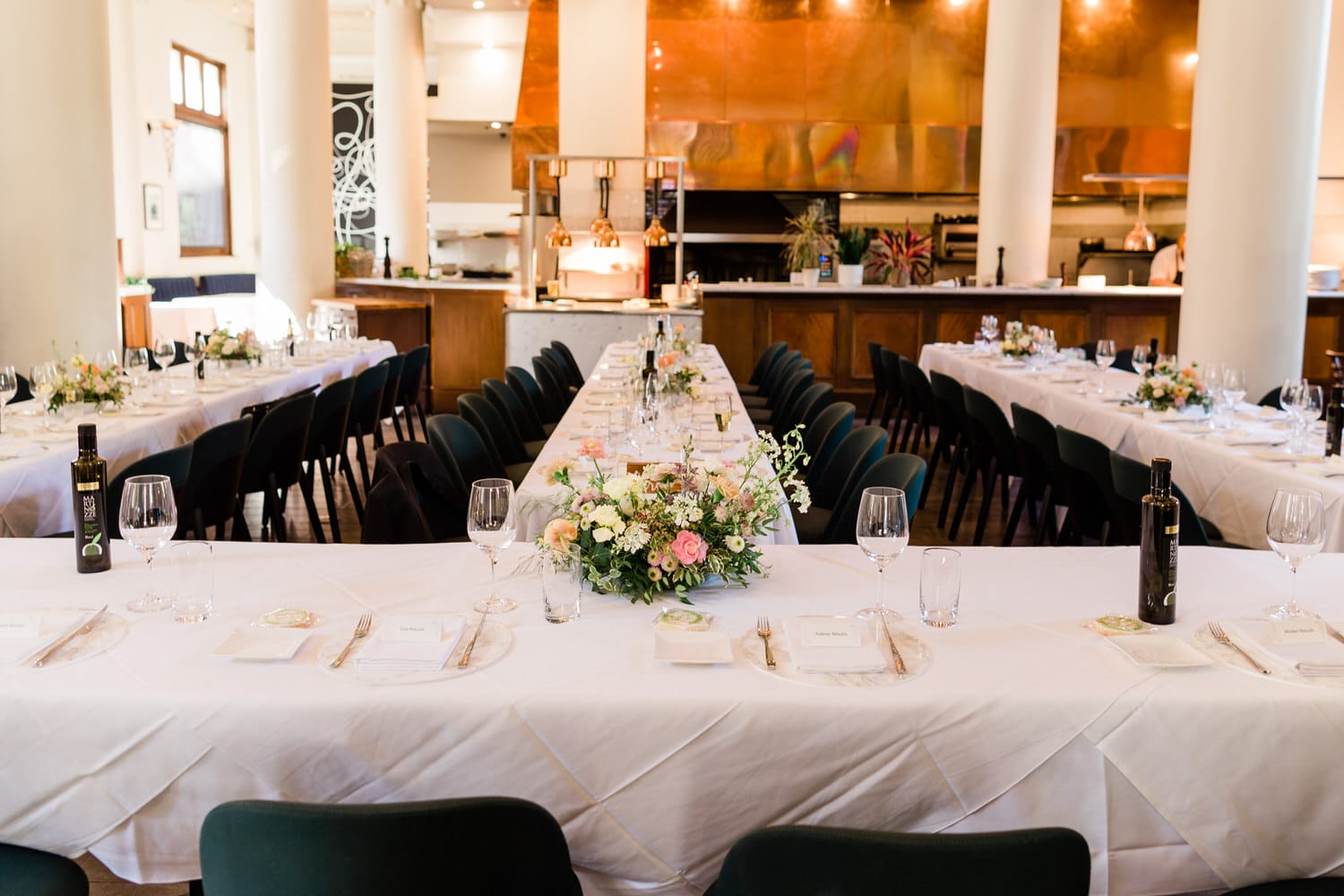 A long dining table elegantly set with flowers, plates, and wine glasses in a stylish restaurant interior