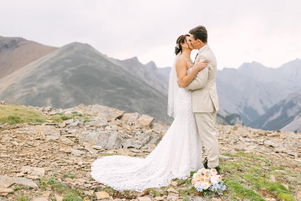 Bride and groom kissing hand in hand on top of a helicopter mountain experience