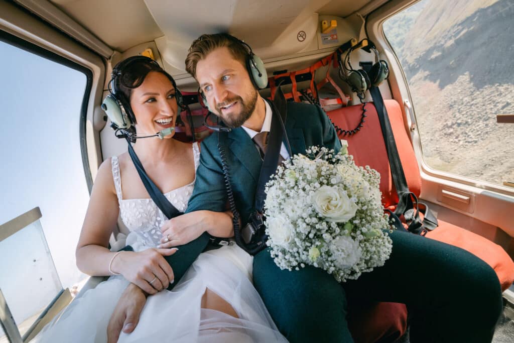 A bride and groom in a helicopter laughing together as they fly to the summit of a mountain which was photographed by Calgary's top wedding photographer Geoff Wilkings