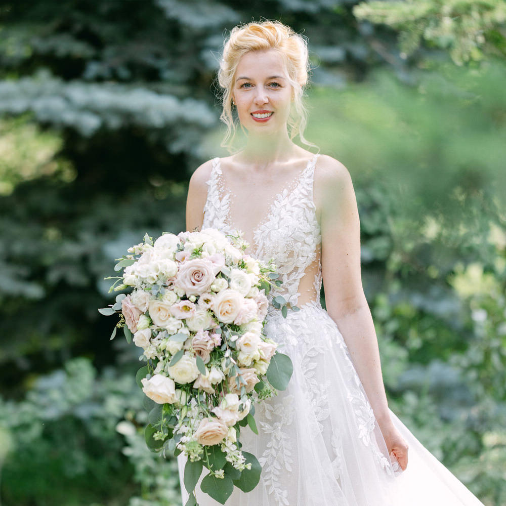 A smiling bride holding a bouquet of flowers, wearing a white wedding dress outdoors.