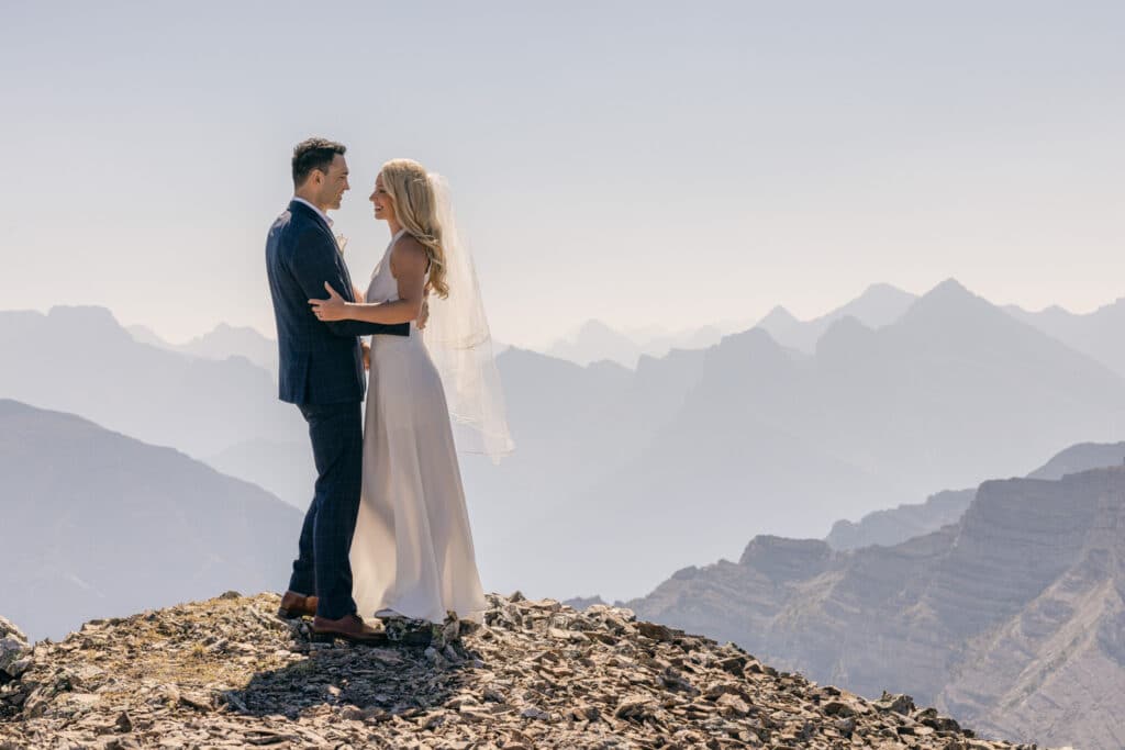 A bride and groom holding each other as they stand next to the mountain edge after just getting married on their mountain eleopement