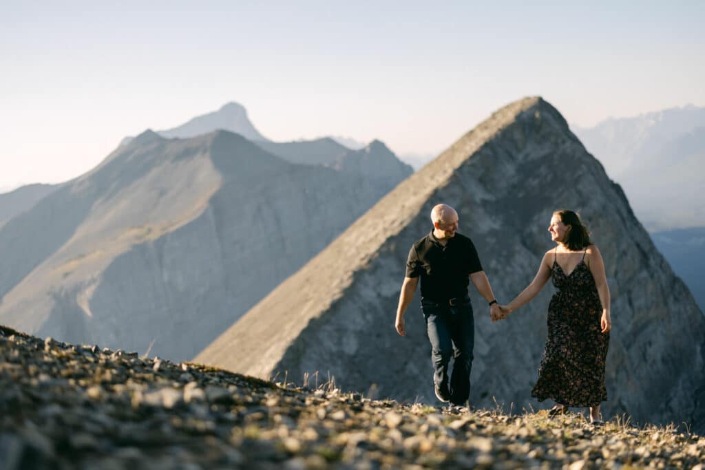 A couple walking in the mountains with a mountain the background during an engagement shoot