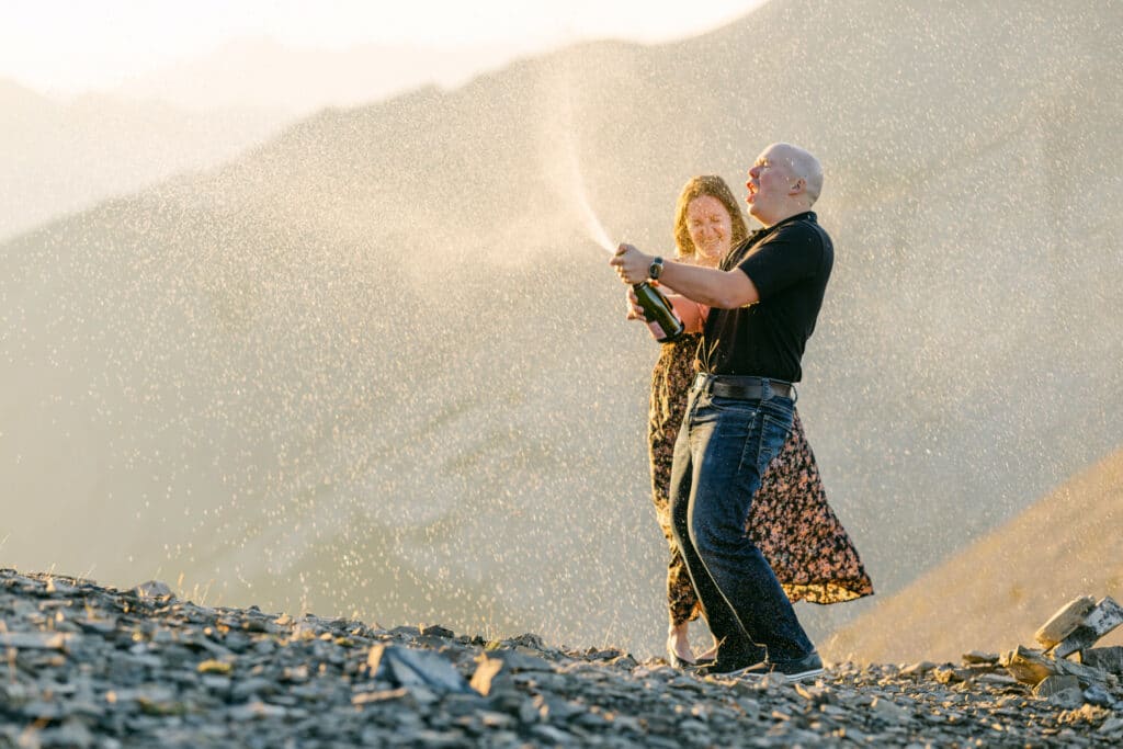 Champagne spraying at the top of a mountain within an engagement shoot