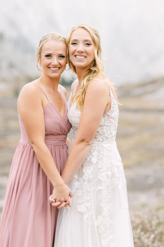 Bride sister holding hands as they look at the camera during a mountain wedding