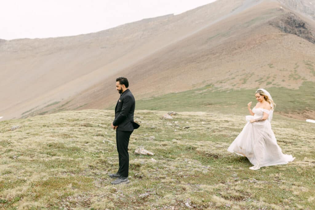 The bride is approaching the groom for their first look high on top of a mountain as they elope