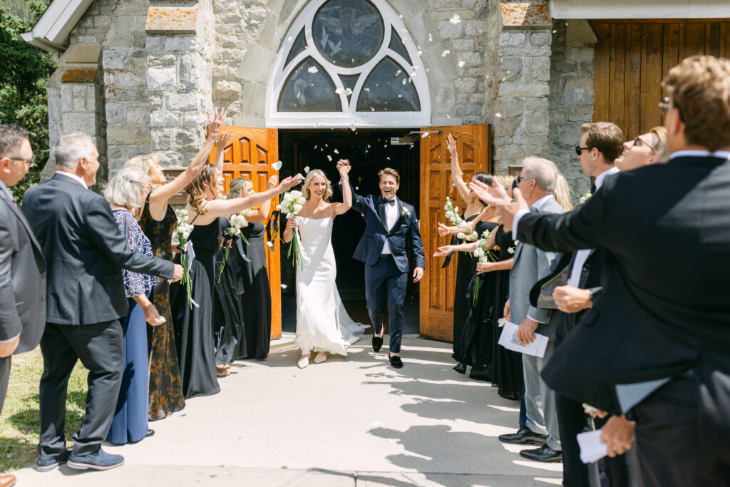 A bride and groom excitedly leaving the church while guests throw flower petals to celebrate their marriage