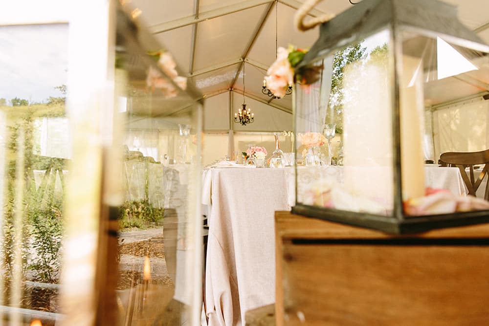 View of a beautifully decorated wedding reception table inside a tent, with floral arrangements and vintage details, seen through a reflective surface.