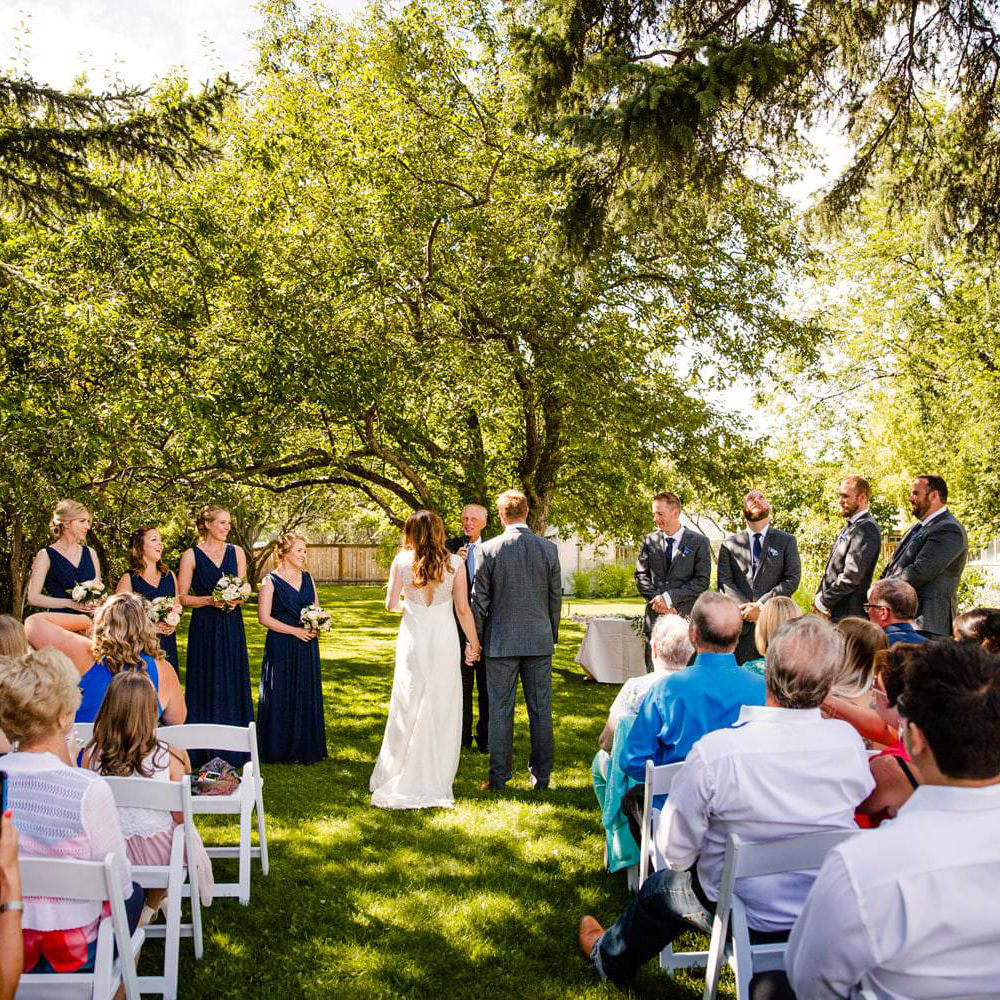 A couple standing at the altar in a garden with guests seated on either side and a bridal party standing nearby.