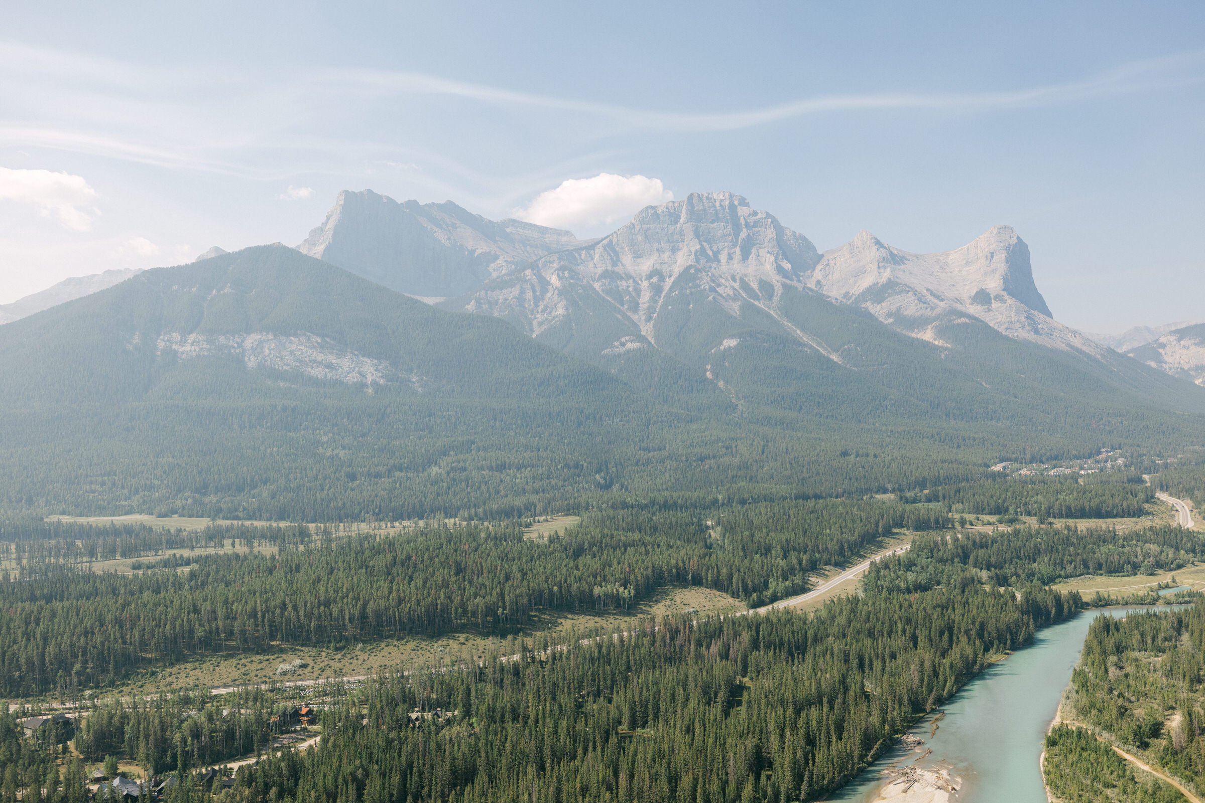 A serene aerial view of a lush forest with a winding river in the foreground and majestic mountains in the background.