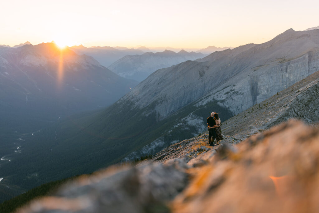 A person taking photos at sunrise on a mountain overlooking a scenic valley and rugged peaks.