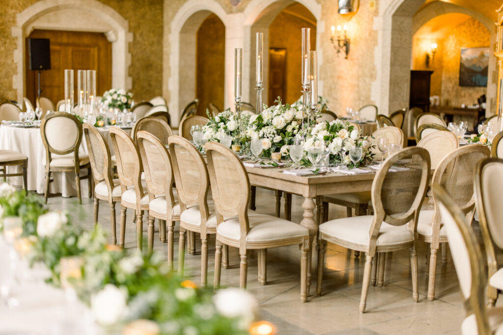 A beautifully arranged wedding reception table with floral centerpieces, elegant dinnerware, and vintage-style chairs in a luxurious venue.