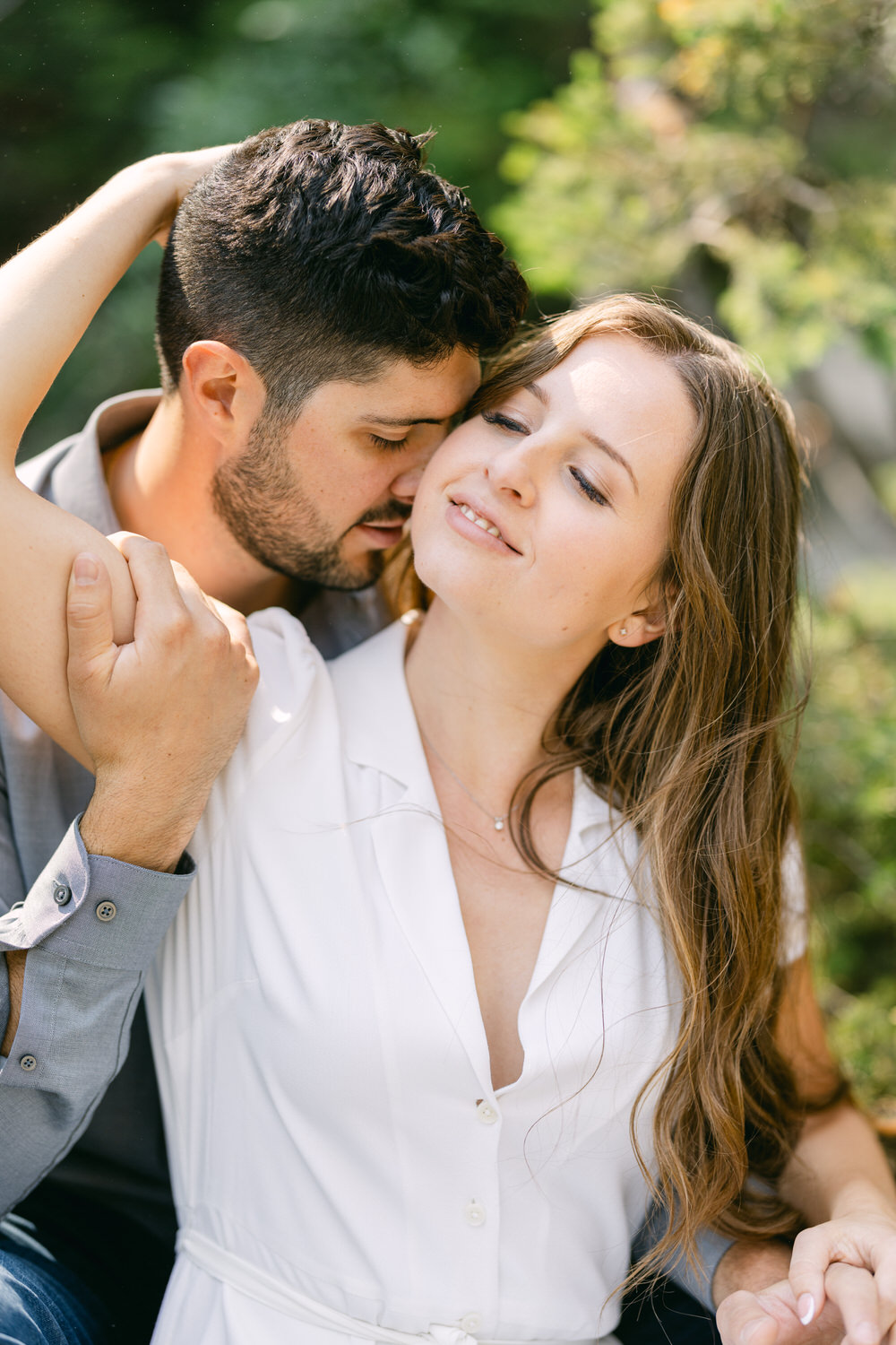 A man and a woman in a loving embrace outdoors, with the man kissing the woman's forehead and a serene expression on the woman's face.