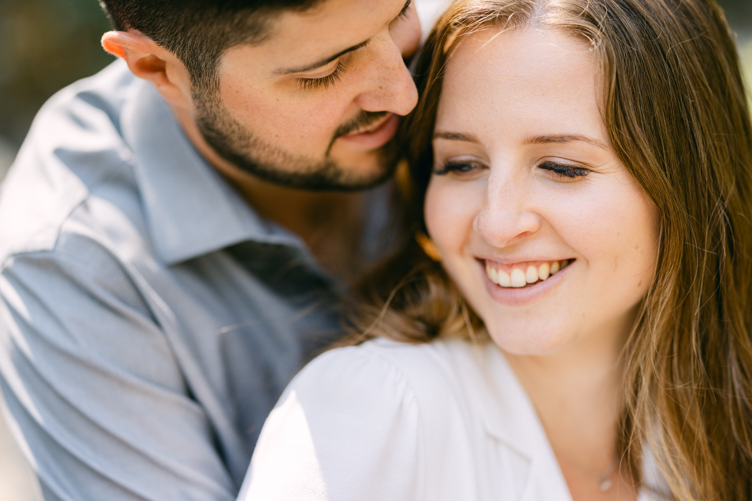 A close-up of a smiling woman with a man leaning in closely behind her, both enjoying a tender and happy moment together.