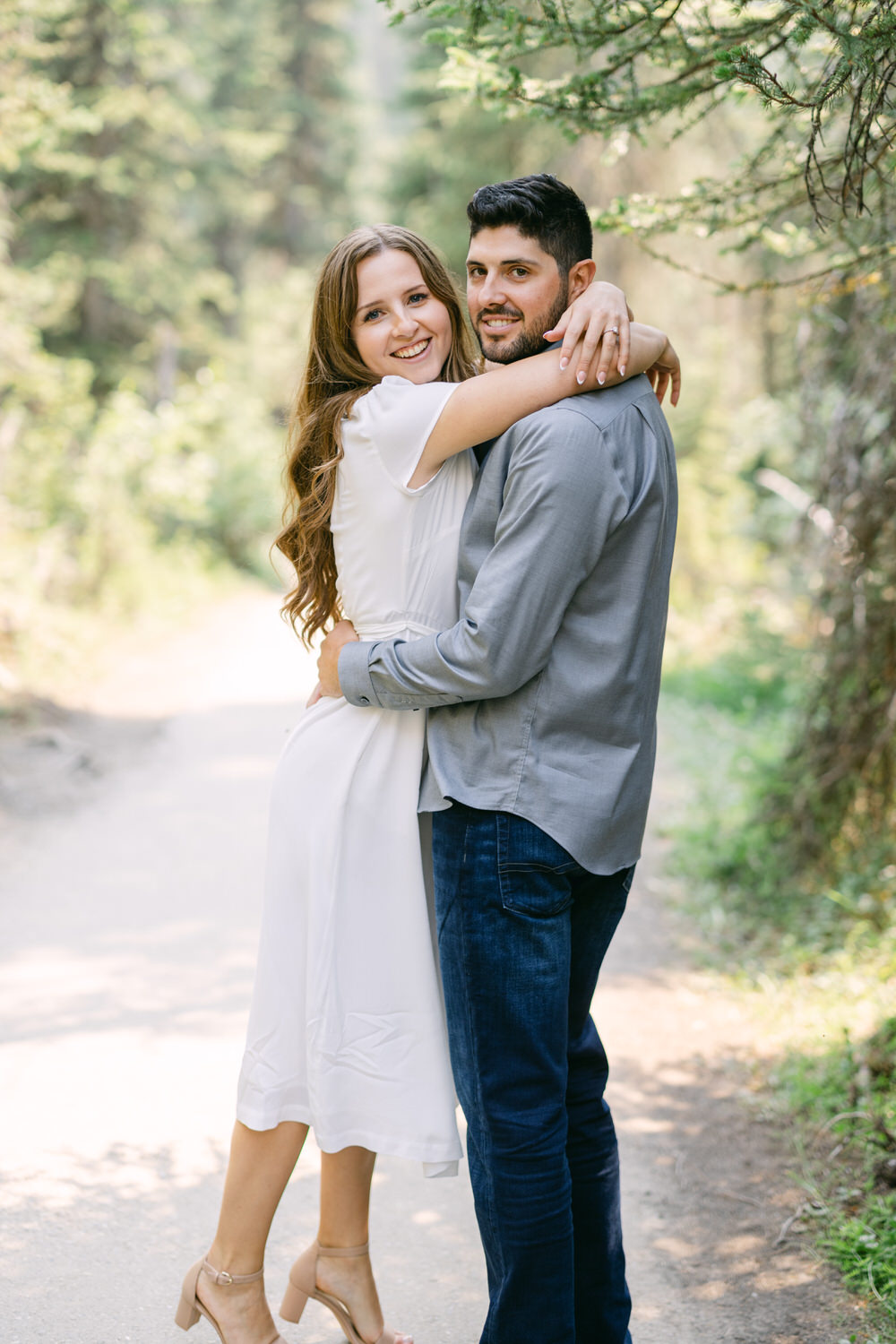 A man and a woman hugging and smiling on a forest path.