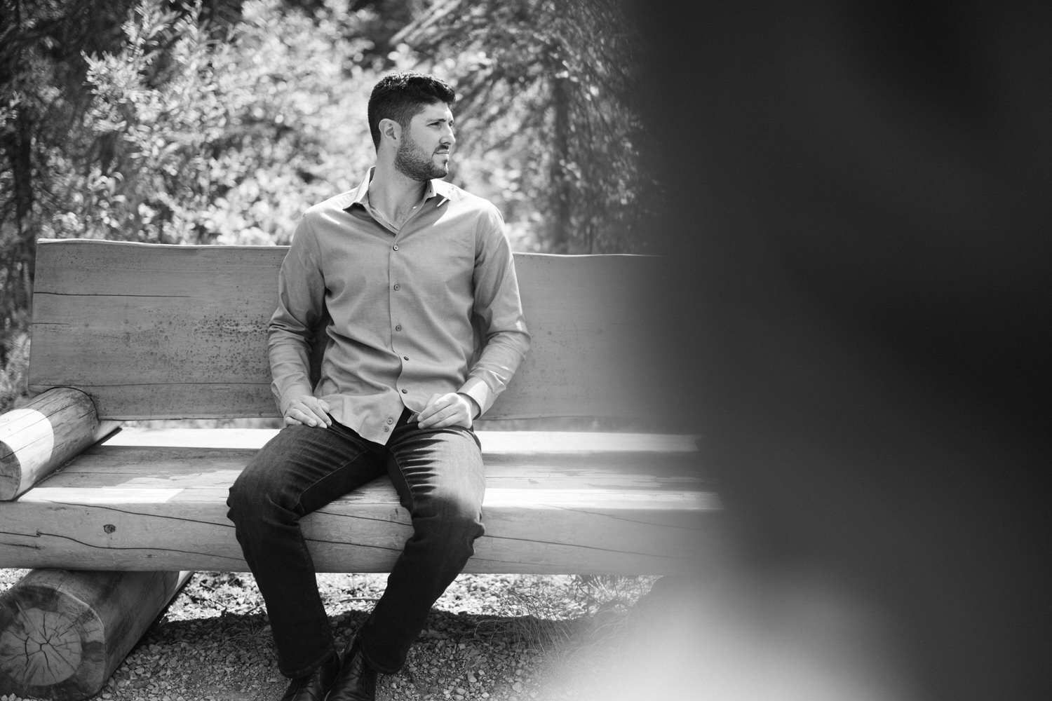 Black and white photo of a man sitting thoughtfully on a wooden bench outdoors.