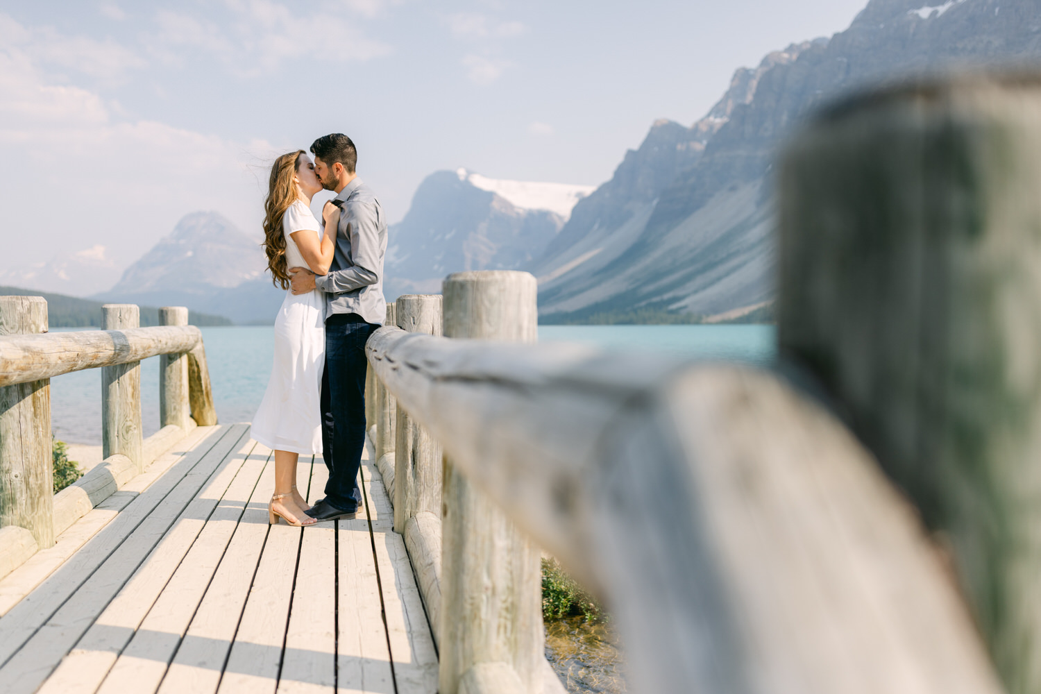 A couple embracing on a wooden dock with a serene mountain lake in the background.