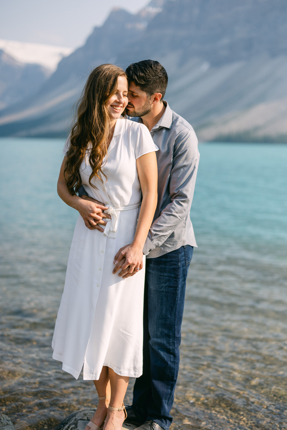 A couple holding hands and sharing an affectionate moment by a clear mountain lake.