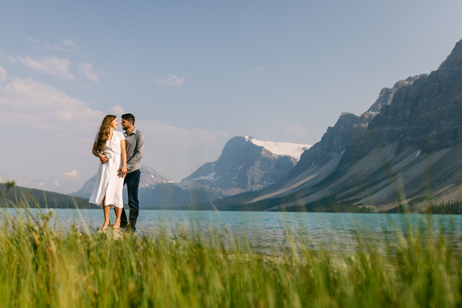 A couple standing by an alpine lake with majestic mountains in the background.