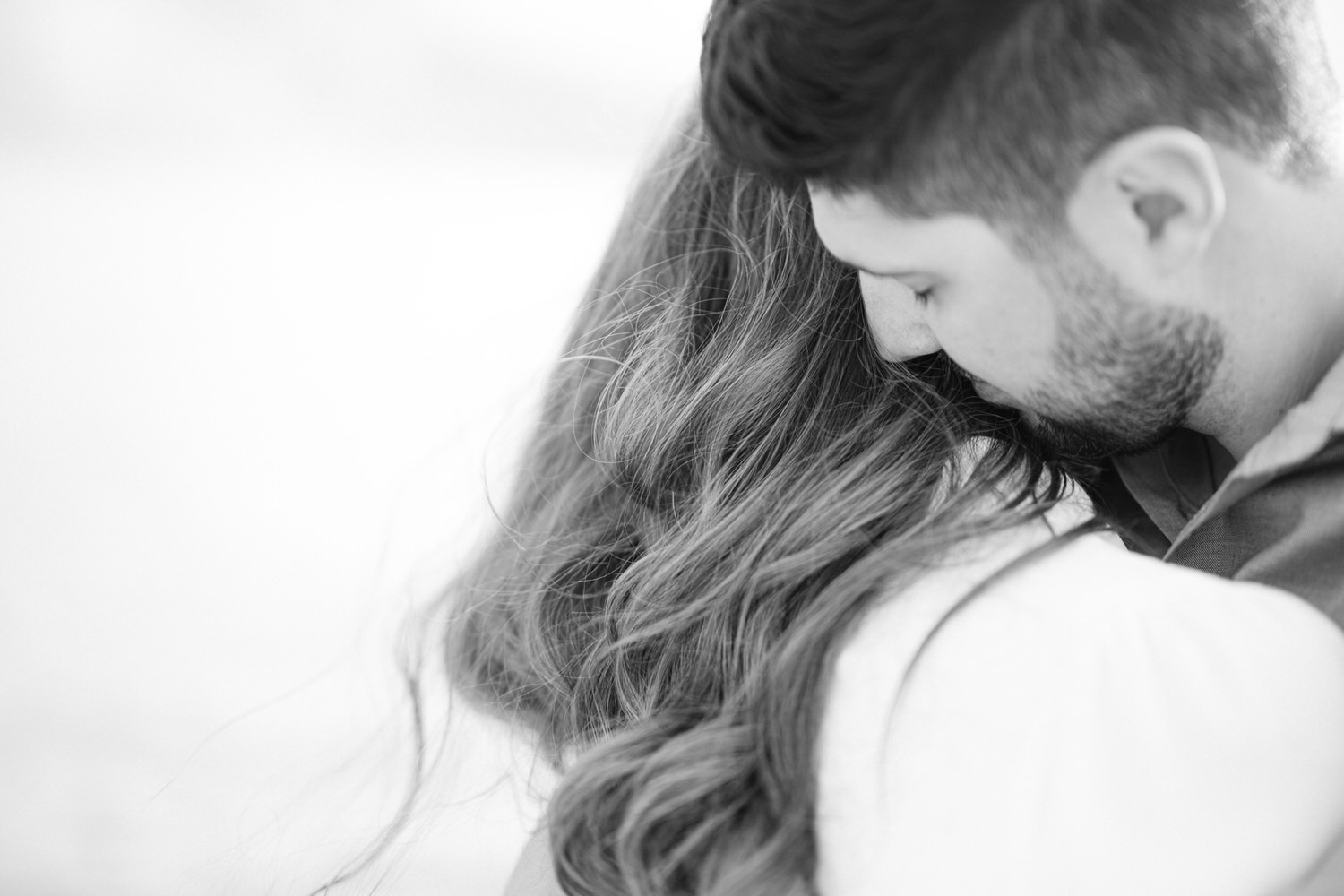 Black and white photo of a man with his head resting against a woman's hair, capturing a moment of closeness.