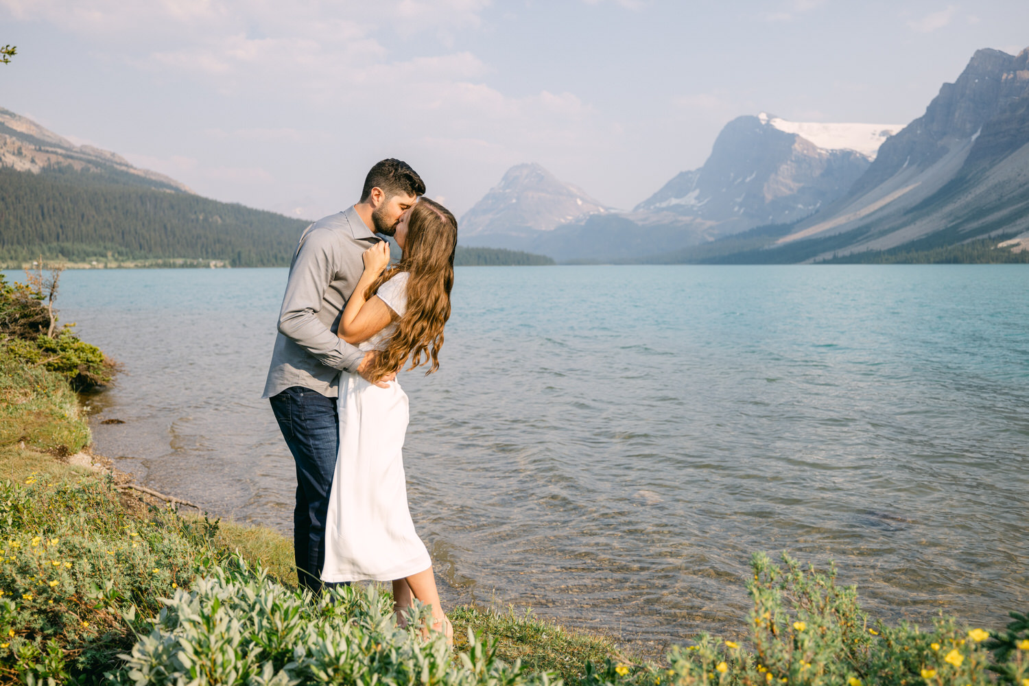 A couple hugging on the shore of a mountain lake with picturesque mountains in the background.