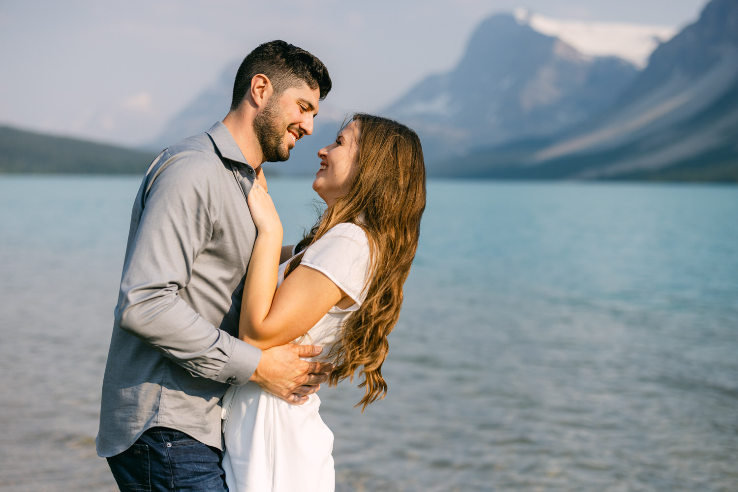 A couple in a loving embrace by a tranquil lake with mountains in the background