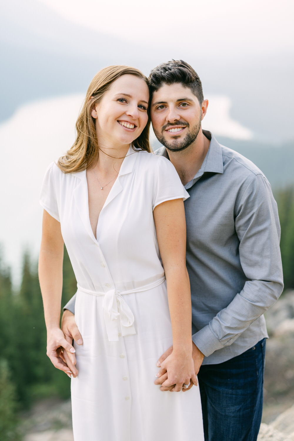 A happy man and woman holding each other, smiling, with a blurred mountainous background.