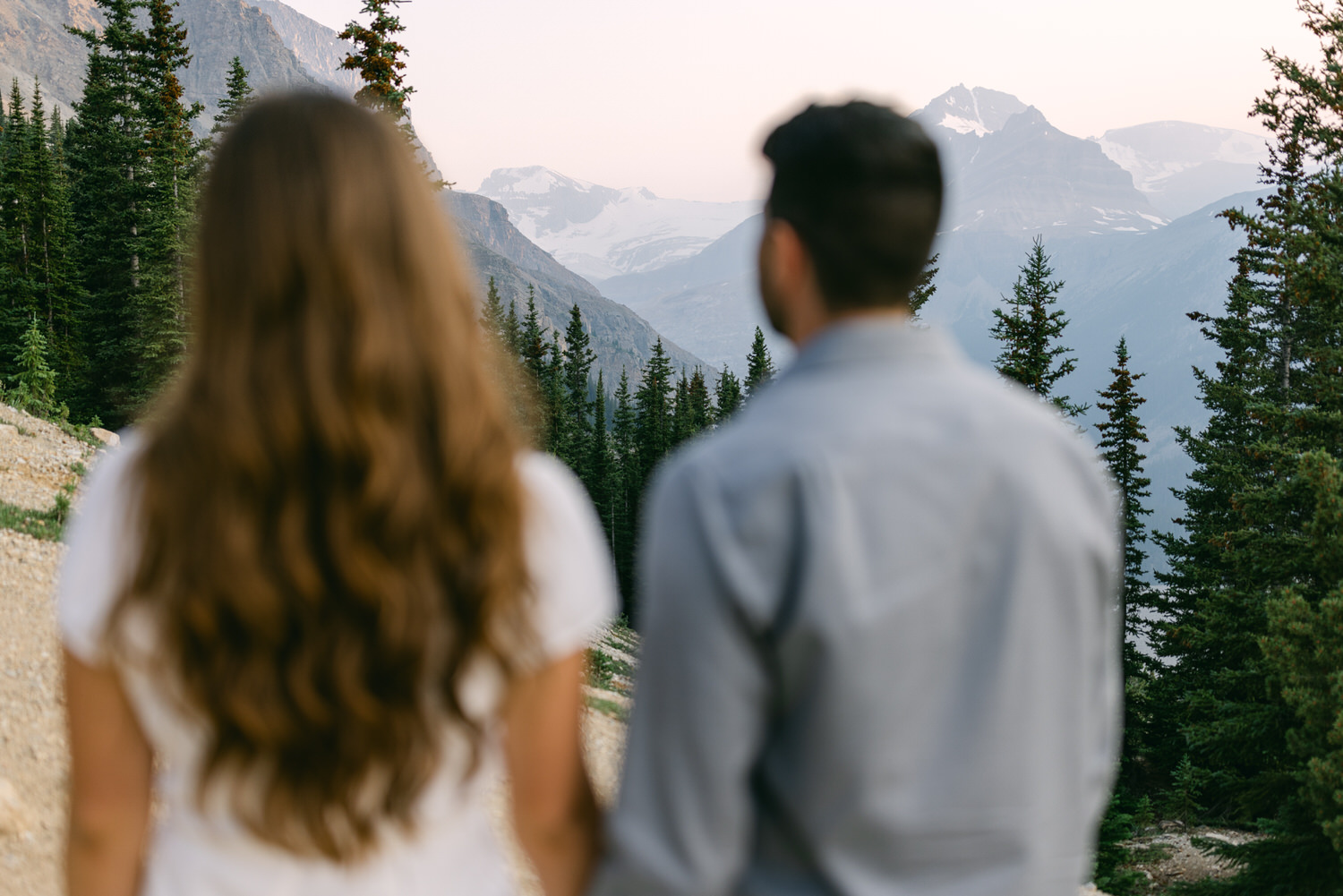 Rear view of a man and woman looking at mountains and forests from a high vantage point.