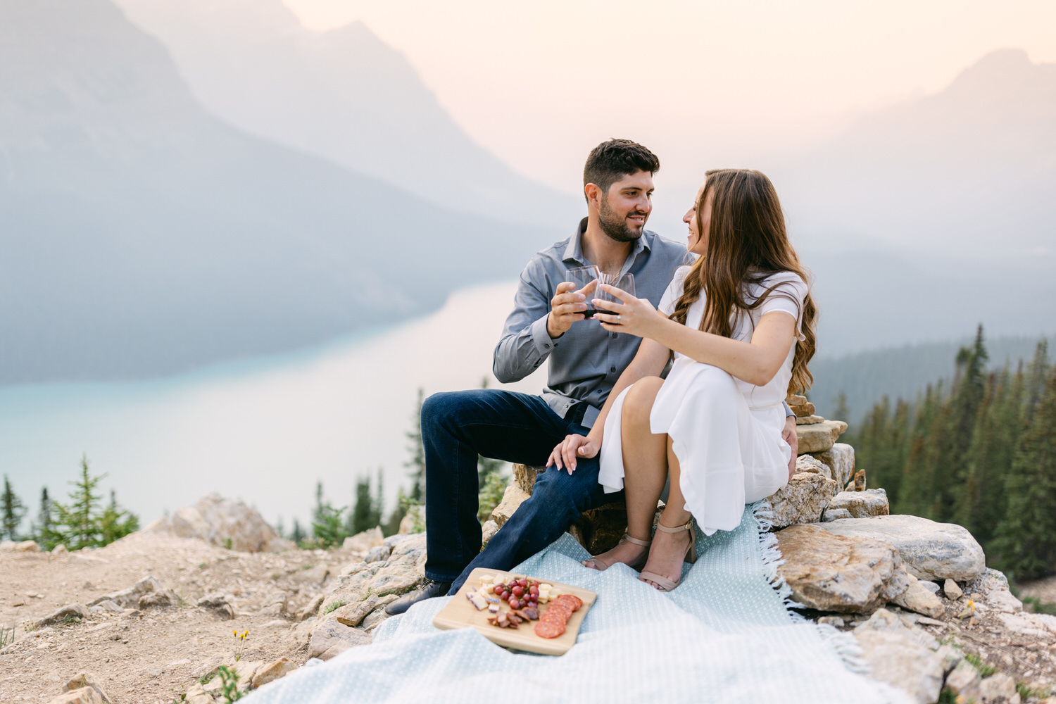 A couple sitting on a blanket enjoying a picnic with a scenic mountain lake background