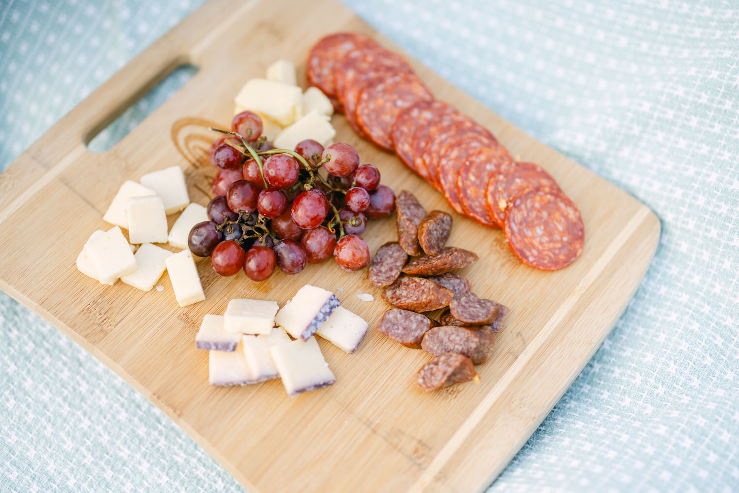 A selection of cheeses, red grapes, and sliced cured meats presented on a wooden cutting board.