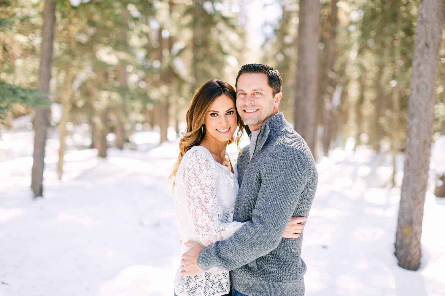 A smiling couple hugging each other with snowy trees in the background