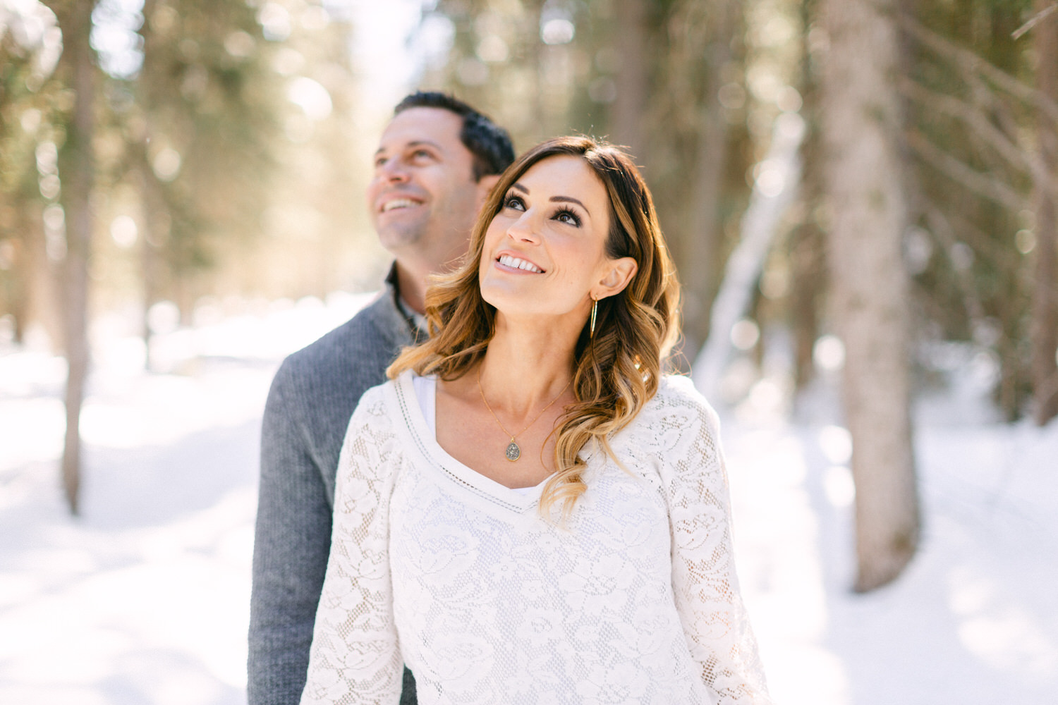 A smiling couple dressed warmly enjoying a sunny day in a snowy forest setting