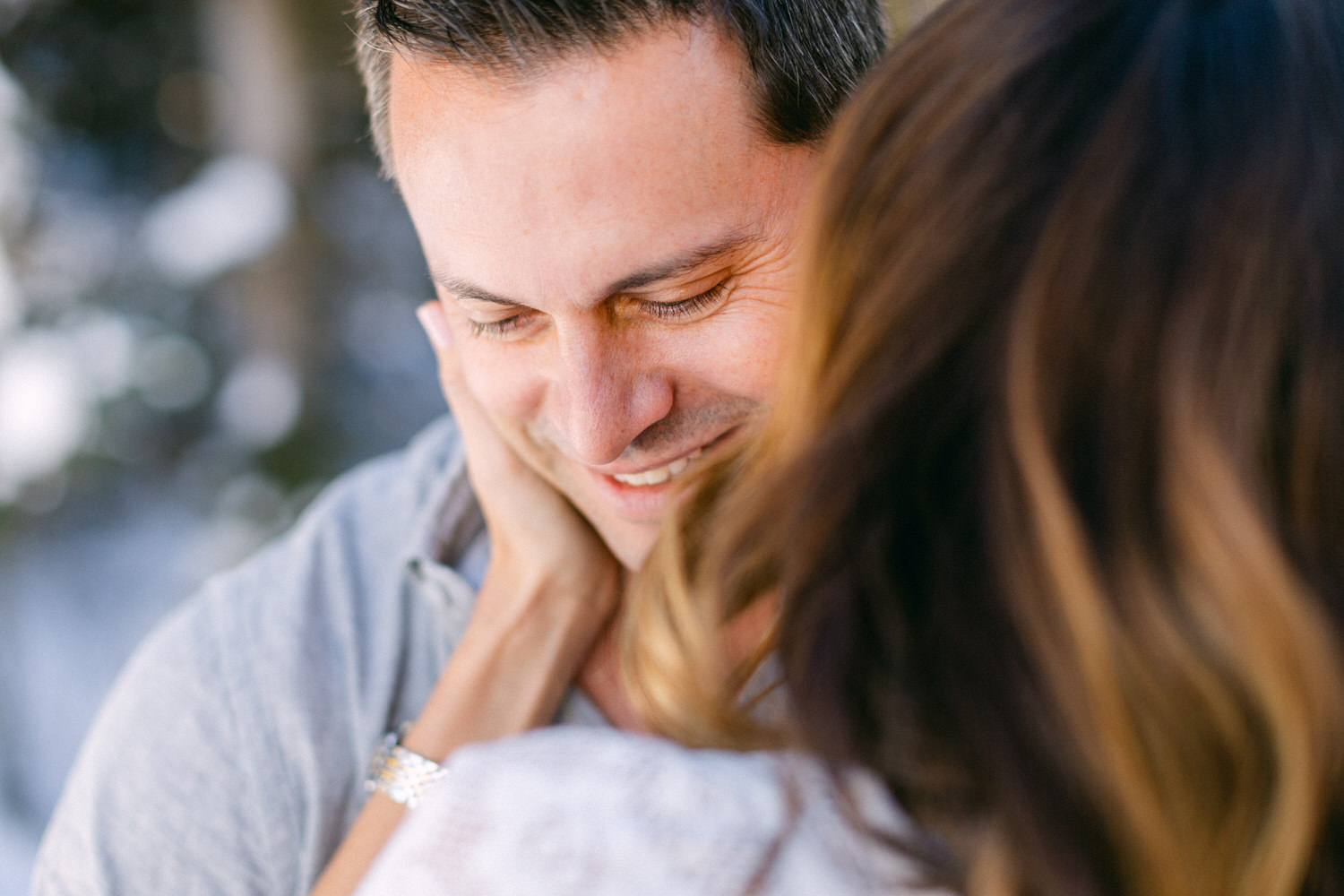 Close-up of a smiling man with closed eyes embracing someone, with focus on the man's joyful expression and a blurred background.