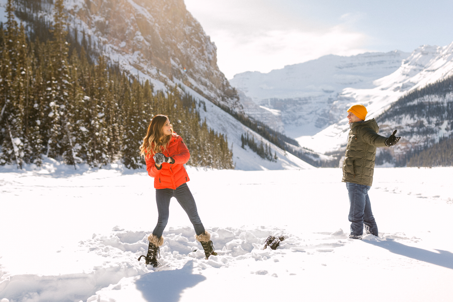 Two people enjoying a snowball fight in a sunny mountainous landscape.