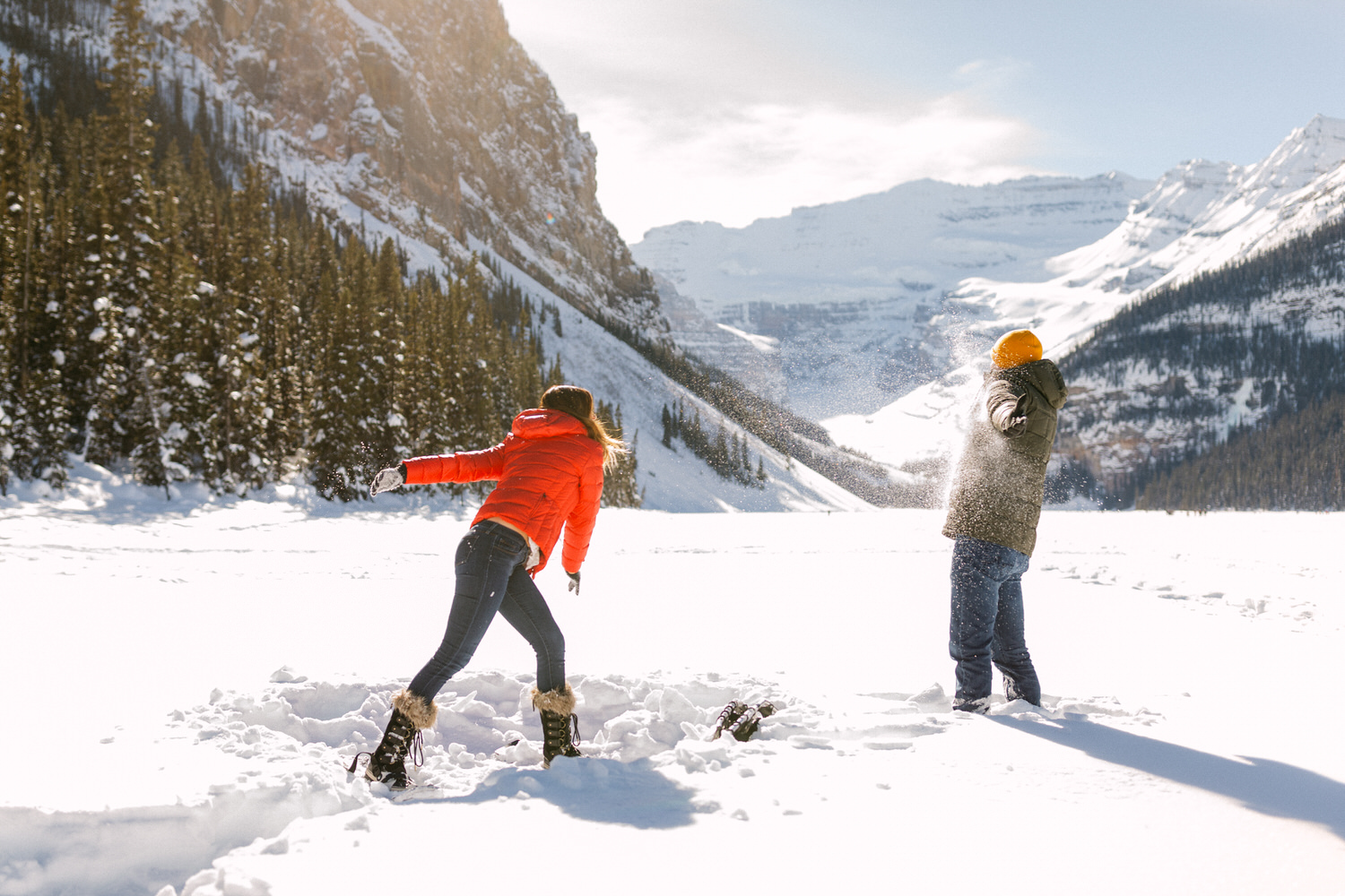 Two people engaging in a snowball fight in a snowy mountainous landscape with clear blue skies.