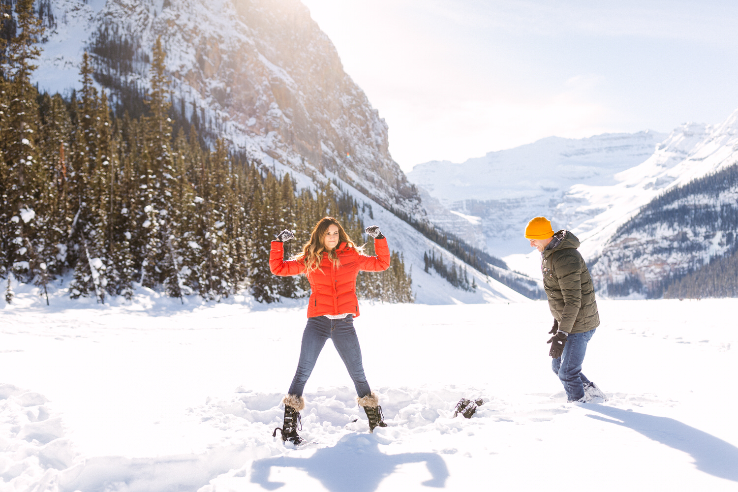 Two people enjoying a sunny day in the snow with mountains in the background.