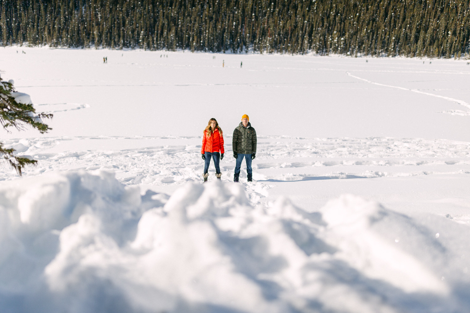 Two people standing in a snow-covered landscape with a forest in the background.