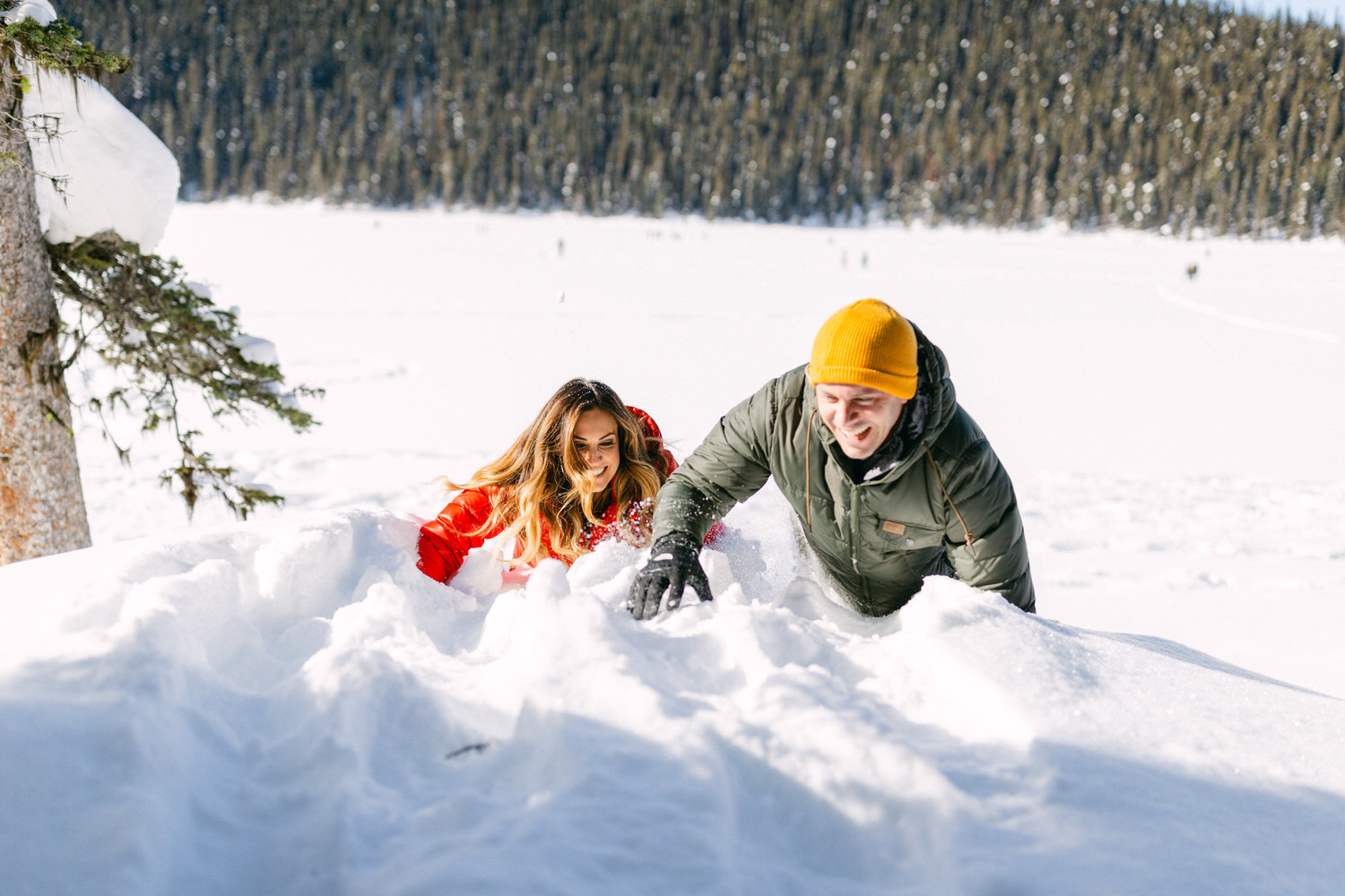 Two people joyfully playing and building with snow in a sunny winter landscape.