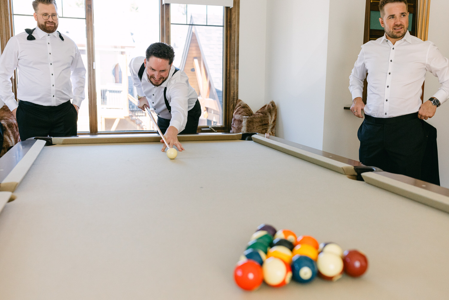 Three men in semi-formal attire playing pool with one of them taking a shot and the others watching.