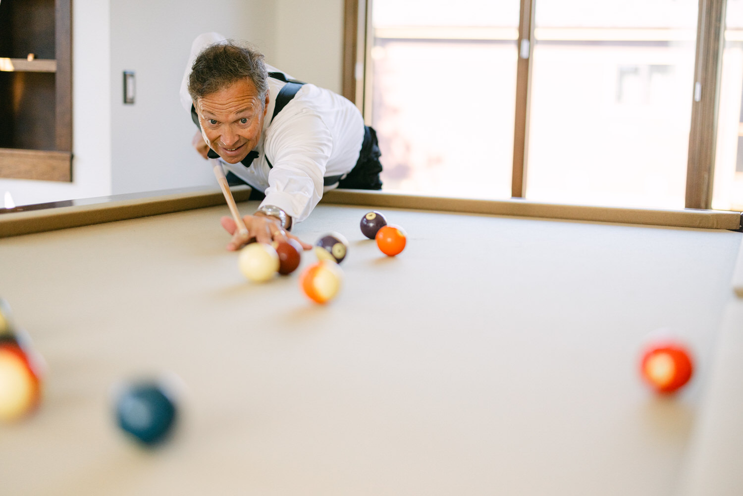 A person is leaning over a billiard table, concentrating on aiming for the cue ball with various colored pool balls in the foreground.