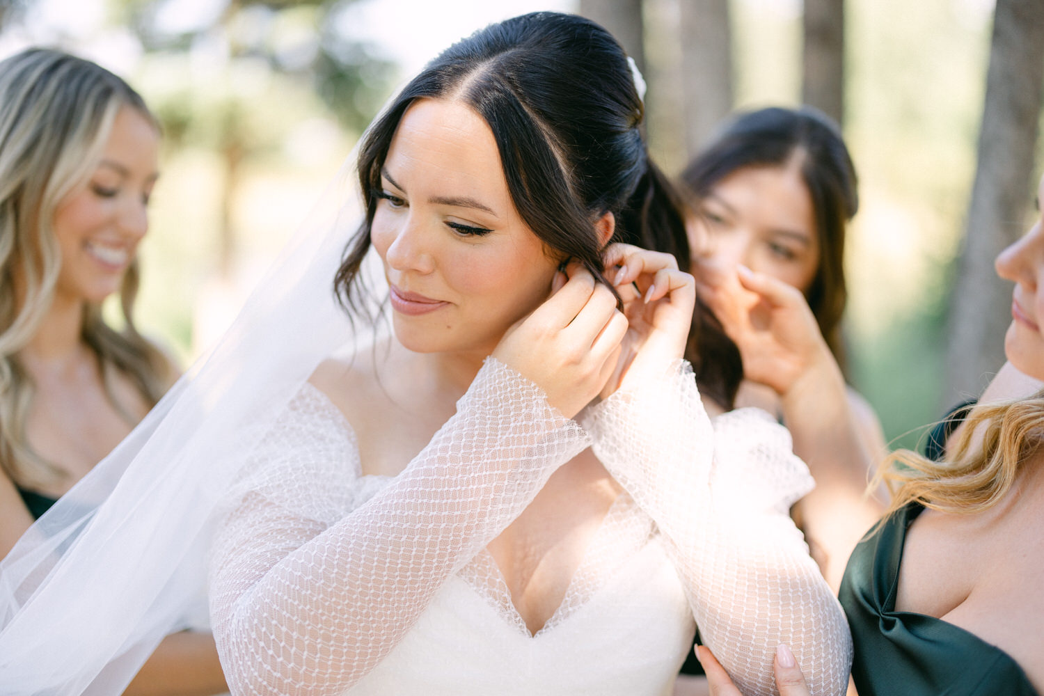 A bride getting assistance with her earrings from bridesmaids before the wedding ceremony.