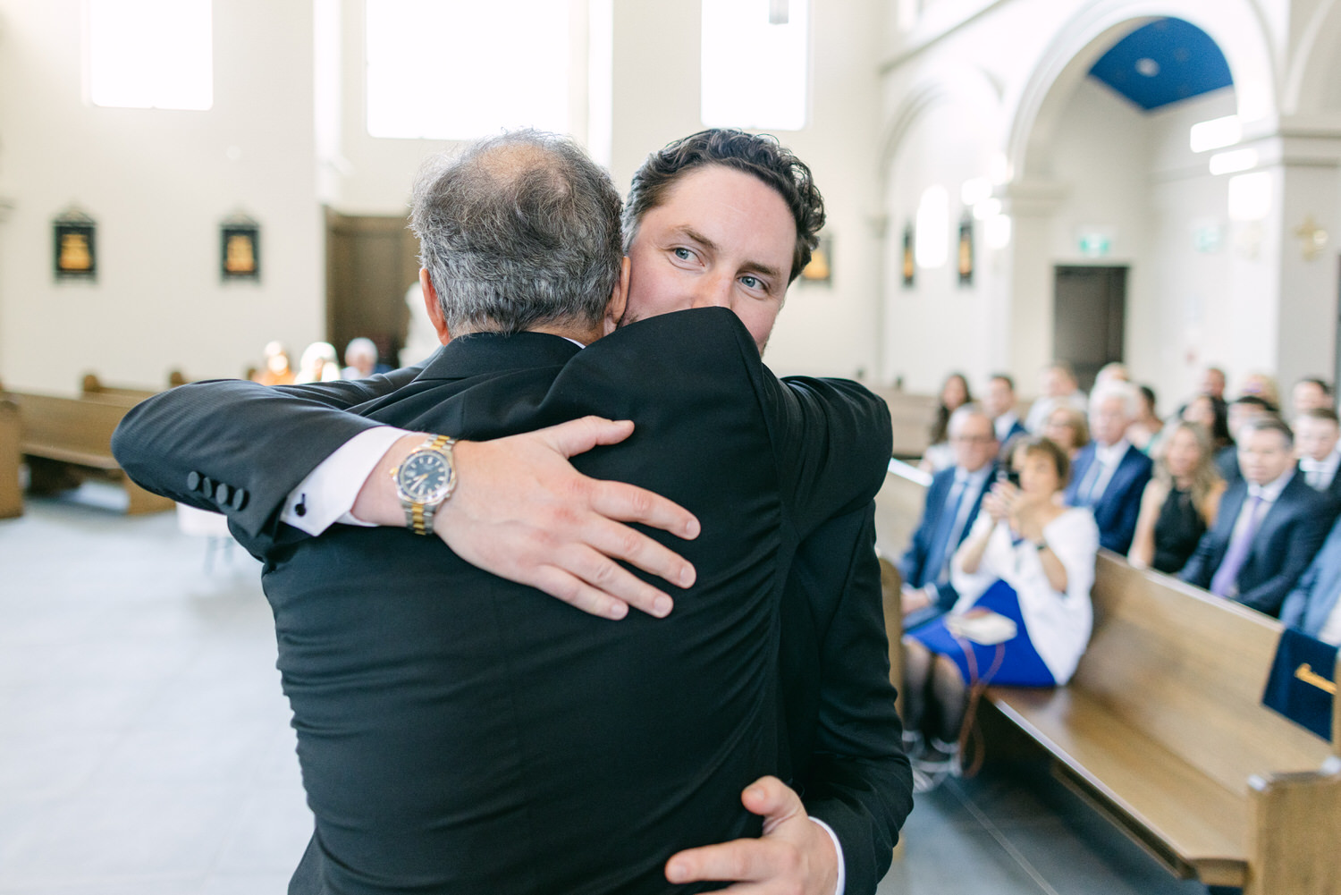 Two men hugging each other at a ceremony inside a church with attendees in the background.