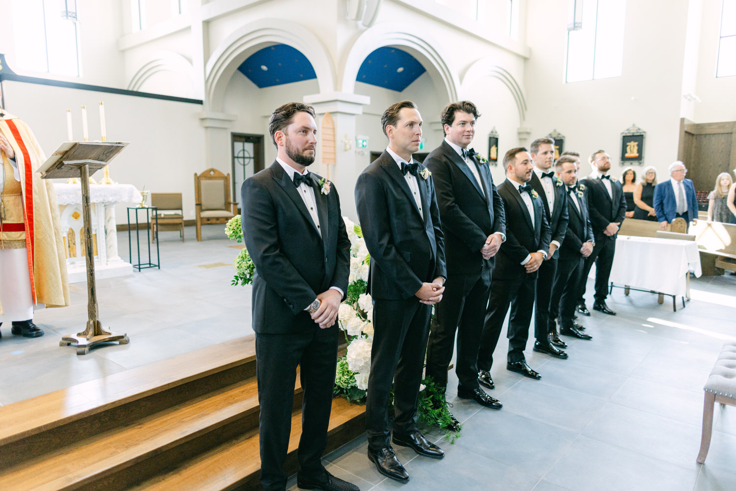 Groom and groomsmen standing in line at wedding ceremony inside a church.