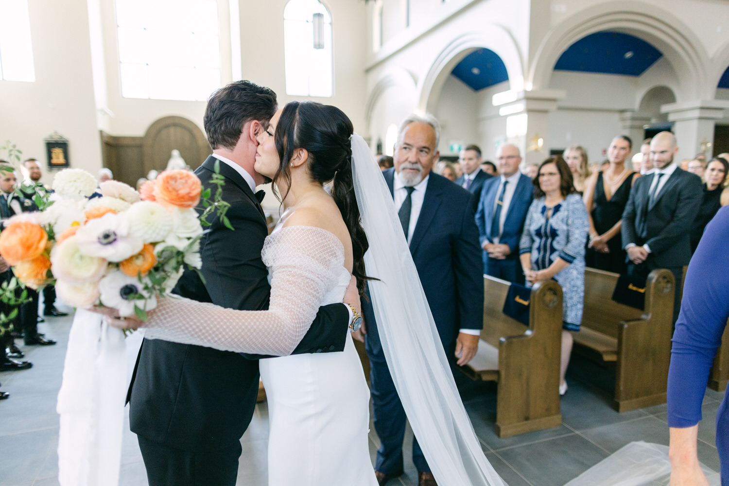 Bride and groom kissing during a wedding ceremony in front of guests at a church.