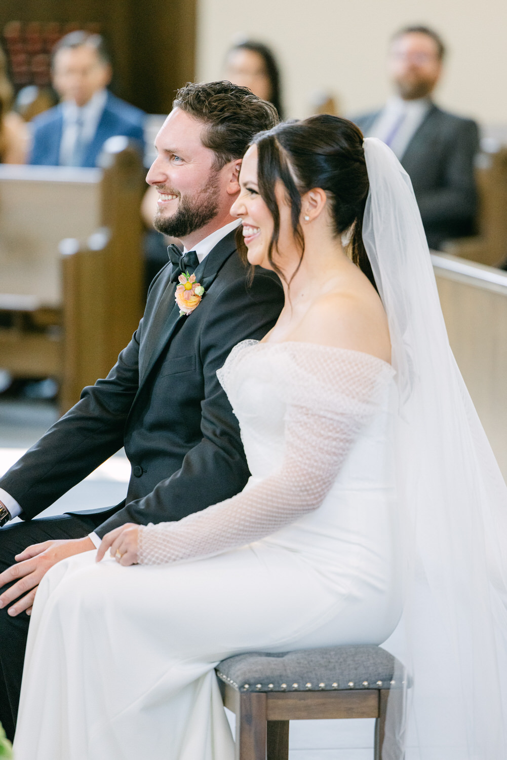 Bride and groom sitting and laughing together during their wedding ceremony inside a church.