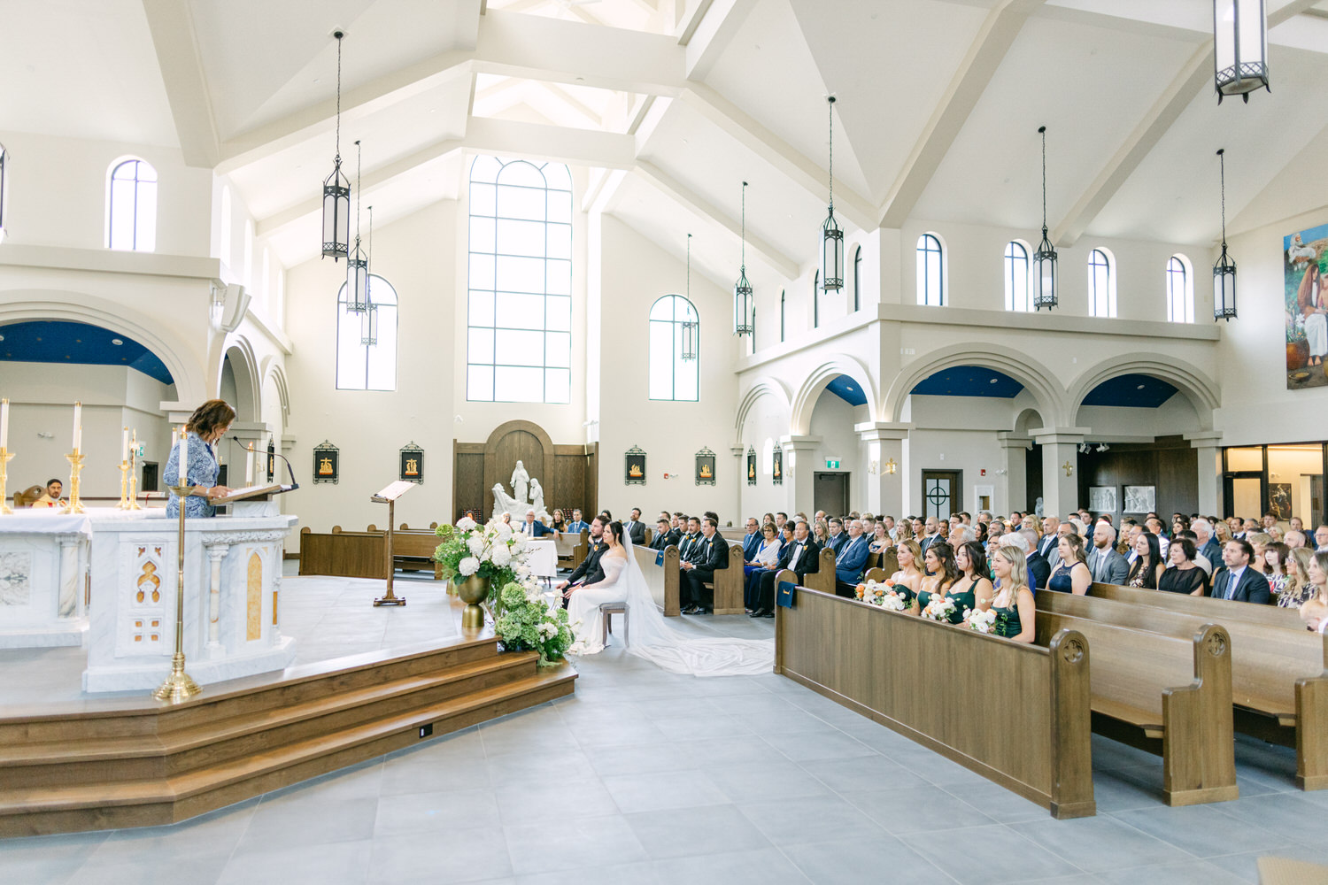 An interior view of a church filled with guests watching a bride and groom during a wedding ceremony, with a speaker at the lectern.