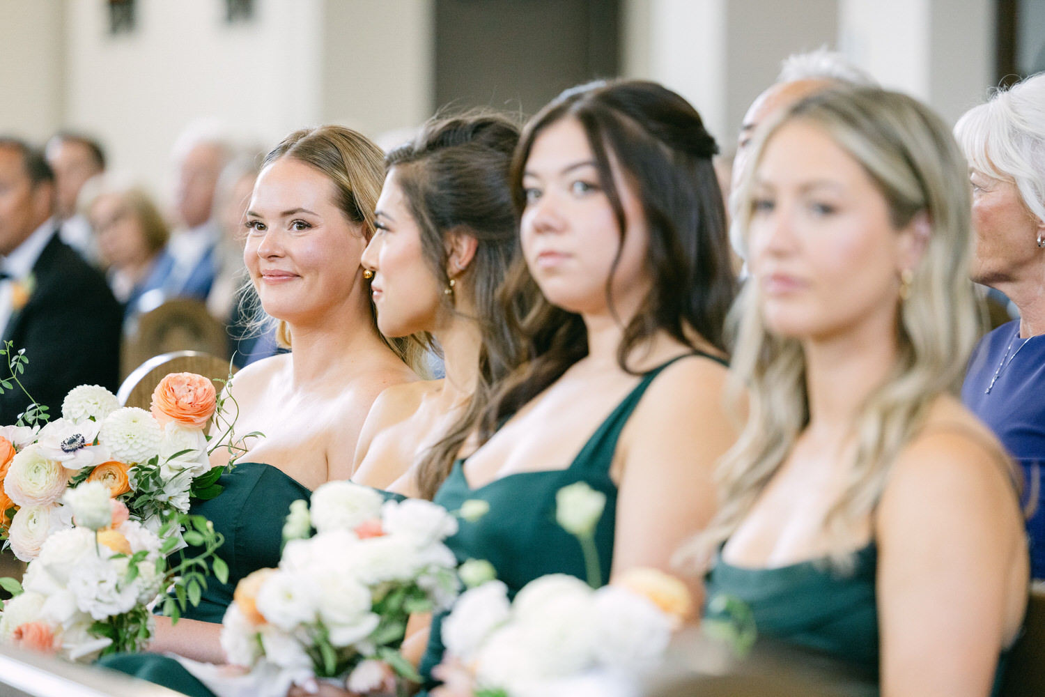 Guests attentively seated with flowers at a formal event, with a focus on women in elegant attire displaying a range of emotions.